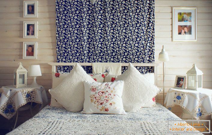 Im Einklang mit dem rustikalen Stil ist das Bett mit einer Anzahl von Kissen mit kontrastierenden roten Stickereien verziert. Nachttische sind mit einer Tischdecke mit zarten blauen Blumen bedeckt.