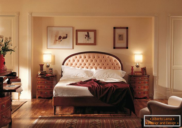 Edler englischer Stil im Schlafzimmer ist attraktiv und bescheiden. Im Mittelpunkt steht ein Bett in einem hohen Kopfteil, das mit einem weichen, hellbeigen Tuch besetzt ist.