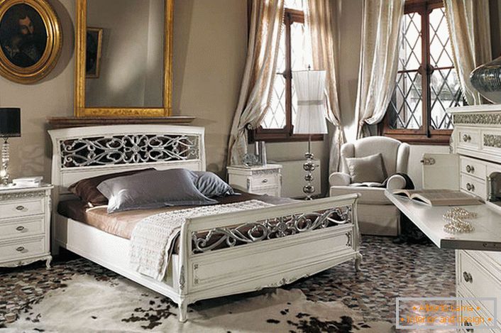 Die Grundvoraussetzung des Barockstils wird beobachtet. In einem geräumigen Schlafzimmer mit hohen Decken kontrastieren weiße Holzmöbel mit den dunklen Fensterrahmen.