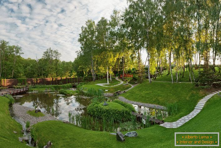 Ein künstlicher Teich hinter dem Haus, der im Stil eines Chalets eingerichtet ist. Eine ungewöhnliche, mutige Lösung für die Gestaltung von Landschaftsdesign.