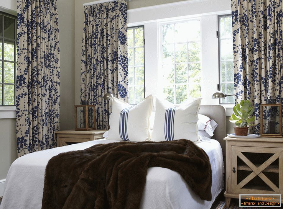 Blaue Blumen auf den Vorhängen und Streifen auf den Kissen sind harmonisch im Inneren des Schlafzimmers kombiniert
