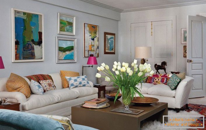 Universal Wohnzimmer im eklektischen Stil. Ein gemütliches Zimmer macht viele Kissen und abstrakte, helle Gemälde, die die Wand über dem Sofa schmücken.