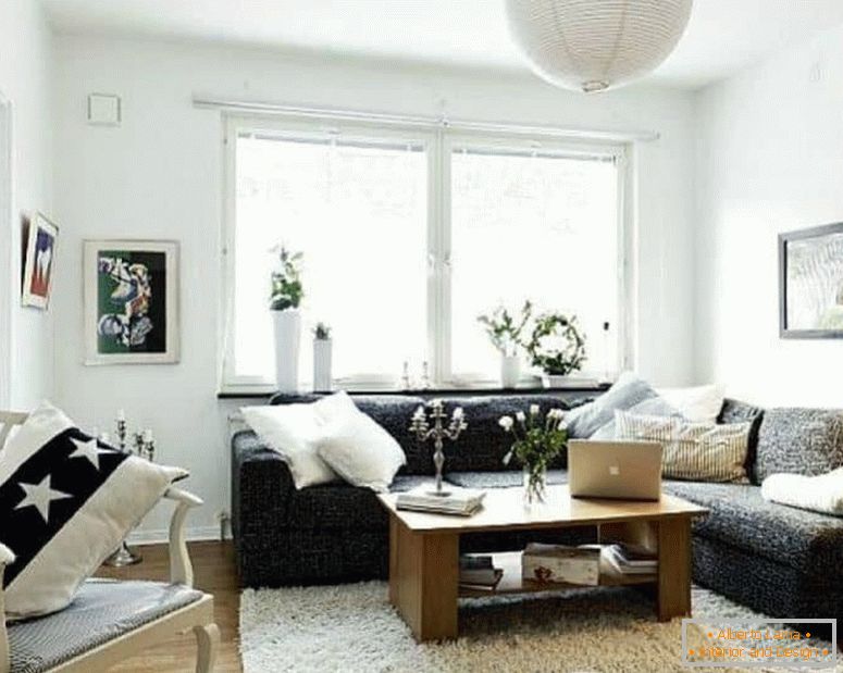 Ein kleines Wohnzimmer in Weiß mit einem dunklen Ecksofa und einem Fenster