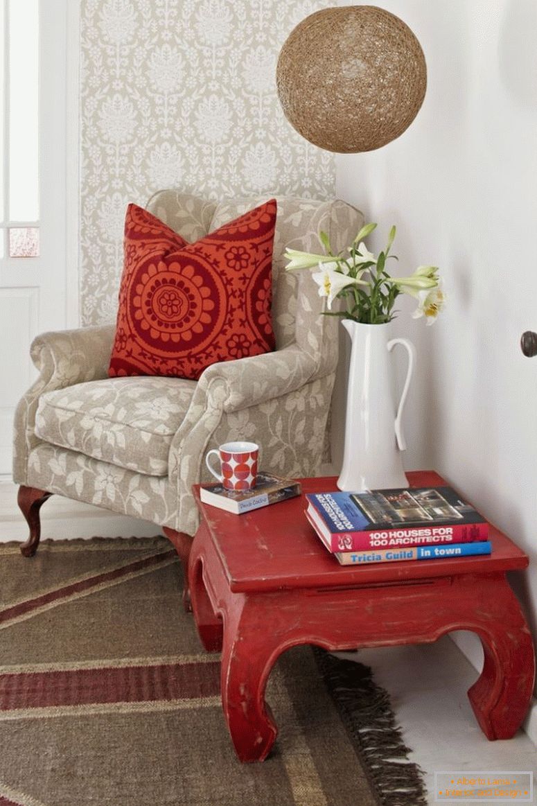 Leseecke; Opiumtisch und blasser Sessel mit gemusterten Kissen an tapezierter Wand