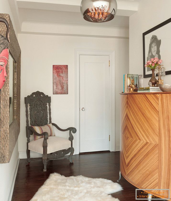 Ein Sessel in der Ecke neben dem Spiegel, ein Bild und eine helle afrikanische Maske an der Wand