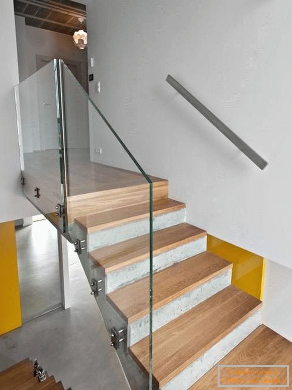 Konkretes Treppenhaus mit hölzernen Schritten und Glasgeländer in einem privaten Haus