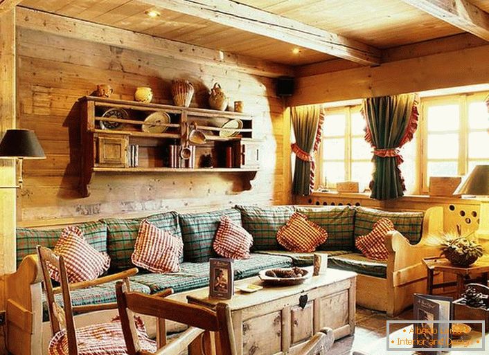 Hölzerne Wanddekoration, kontrastierende Kissen auf einem weichen Sofa, dichte Vorhänge mit Rüschen an den Fenstern. Gemütliches Wohnzimmer im rustikalen Stil in einem Landhaus.