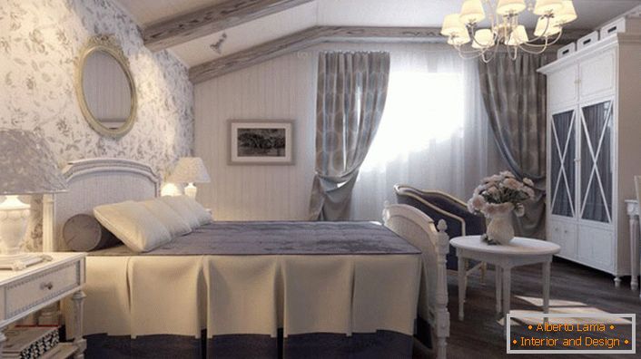 Das Schlafzimmer im Landhausstil ist in gedeckten Blautönen gehalten. Die Wand am Kopfende des Bettes ist mit Tapeten mit Blumenmuster bedeckt.