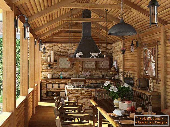 Eine kleine Küche mit einem Grill auf der Veranda eines Landhauses. Der Landhausstil zeigt sich vor allem an der Dekoration der Wände und der Decke mit einem Holzrahmen.